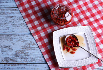 Goji berry jam in spoon on plate with jar on table close up