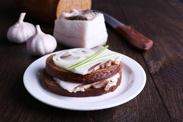 Sandwiches with lard on plate and garlic on wooden background