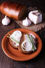 Sandwiches with lard on plate and garlic on wooden background