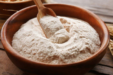 Flour and grains in bowls with ears on wooden background