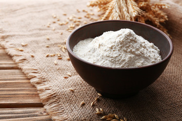 Flour in bowl with ears and grains on sackcloth background