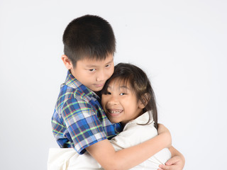 Loving brother and little sister hugging on gray background.
