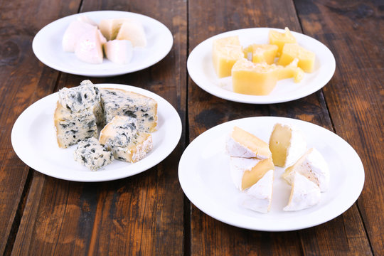 Various types of cheese on plates on wooden table background