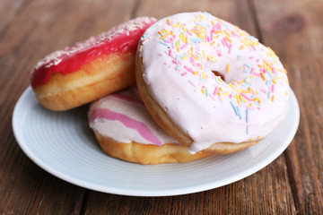 Delicious donuts with icing on plate on wooden background