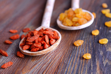 Raisins and Goji in spoons on rustic wooden table background