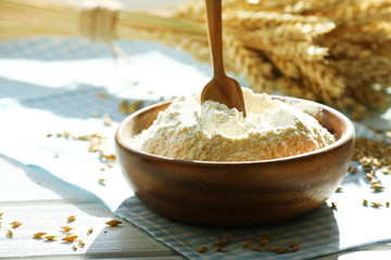 Bowl of flour with spoon and napkin on wooden table, closeup