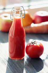 Bottle of tomato juice with fruits and vegetables on windowsill