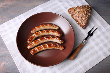 Grilled sausages on plate with bread on table close up