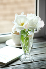 Book with cup of tea and white tulips in vase on windowsill