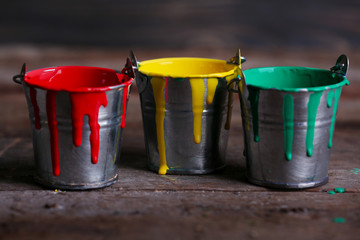Metal buckets with colorful paint on wooden background © Africa Studio