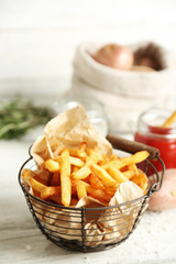 Tasty french fries in metal basket on color wooden background