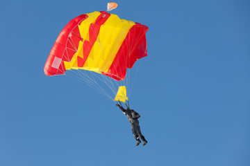 Skydiver flies on red yellow parachute. Blue sky