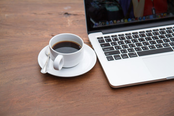 Black coffee in a white cup on a table with a computer.