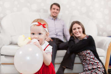 Baby girl with balloon and father and mother in domestic room