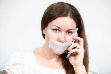 Woman with cellphone, tape on mouth, grey background