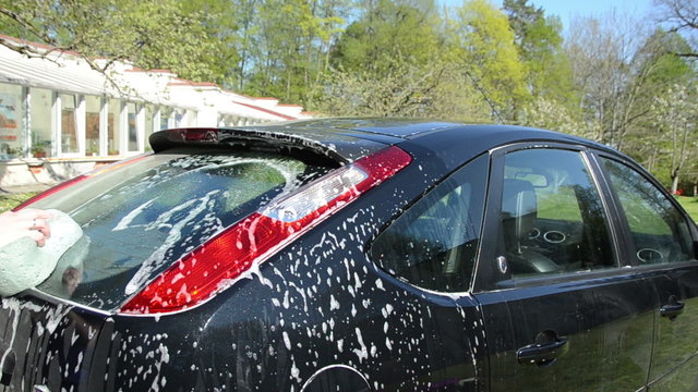 Closeup of man wash black favorite car with foam and sponge