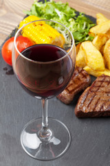 Red wine glass and steak with grilled potato, corn, salad