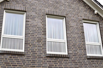 Drei Fenster mit geschlossenen Gardinen an einer modernen Hauswand