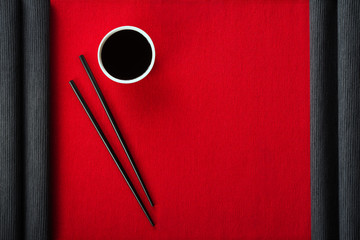 Chopsticks and bowl with soy sauce on cotton mat top view