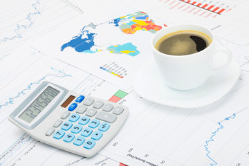 Coffee cup and calculator over financial charts - studio shot