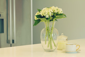 Glass vase of white flowers and teacup in a kitchen with blurred