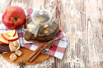 Ripe apple, cinnamon and fruit drink in glass teapot on wooden