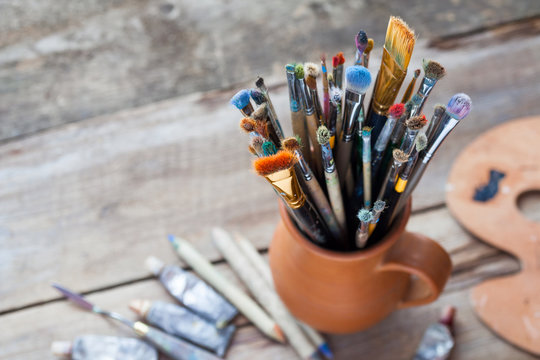 Paintbrushes in a jug from potters clay, palette and paint tubes