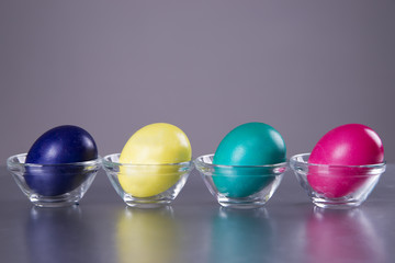 Four colored eggs in a cup on a gray background