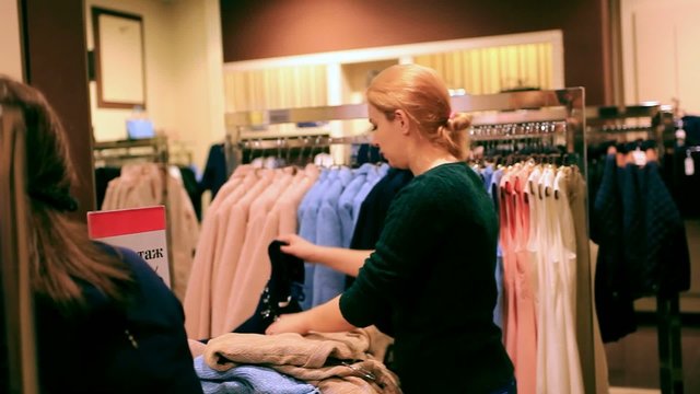 Two young women chooses some clothes at shop of fashionable