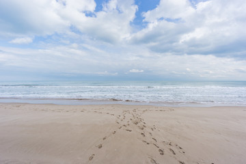 Fototapeta na wymiar Footprints on the beach sand. Wide angle with sea and clouds