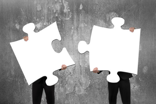 Two business people assembling white jigsaw puzzles with concret
