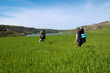 Fototapeta na wymiar Men and girl with backpacks in deep green grass near sea