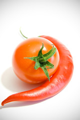 chili peppers and tomato next to each other on a white backgroun