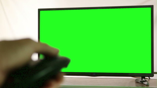 Male hand with TV remote switching channels on green screen