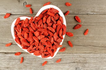 Heart shaped bowl filled with goji berries over wood