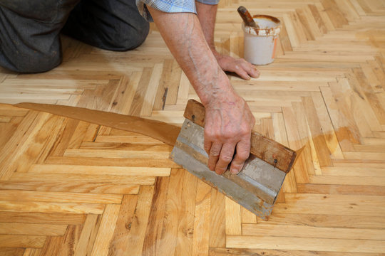 Varnishing of oak parquet floor, senior workers hand and tool