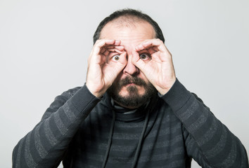 Shocked man looking through hands, making binoculars