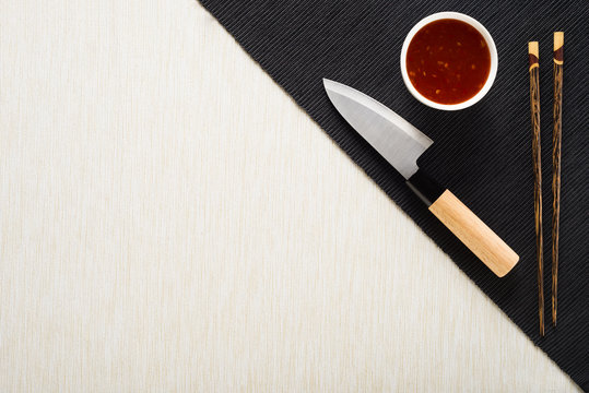 Chopsticks, Knife And Bowl With Sauce On Table Mat Top View