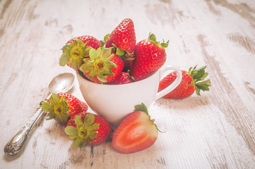 Spring fruits, strawberries in a white cup on a vintage wooden t