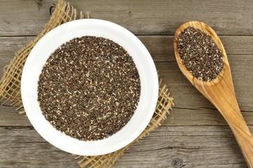 Bowl and spoon filled with chia seeds over a wood background