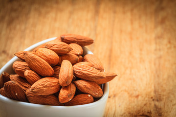 Almonds in bowl on wooden background