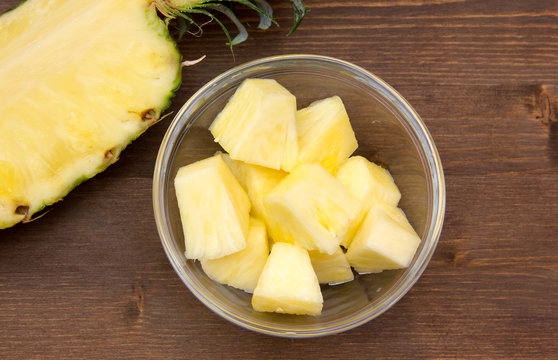 Pineapple cubes on bowl on wooden table seen from above