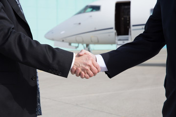 Businessmen shake hands in front of a corporate jet