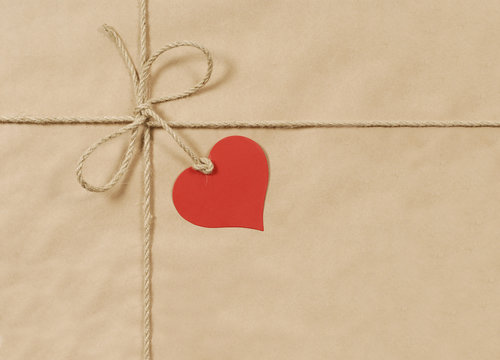 Brown paper package parcel background tied with string or rope and blank red heart shape message tag or label photo