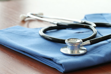 Stethoscope with blue doctor coat on wooden table with shallow D