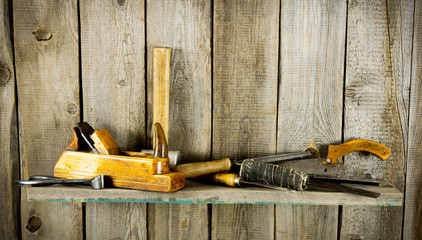 Many old tools (plane, mallet and others) on a wooden shelf.
