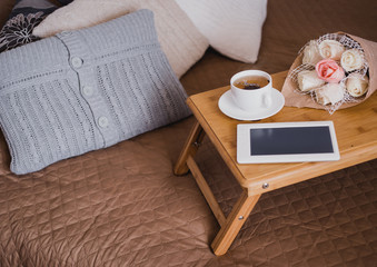 Wooden tray with tea, flowers and e-book standing on a bed