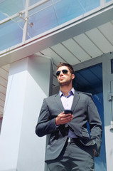 attractive young businessman with phone device on office buildin
