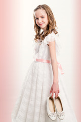 Cute Communion girl holding shoes.