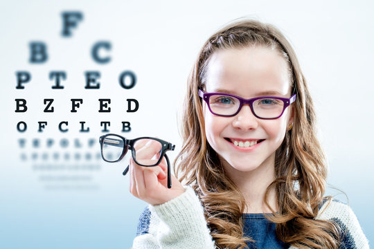 Girl holding glasses with test chart in background.